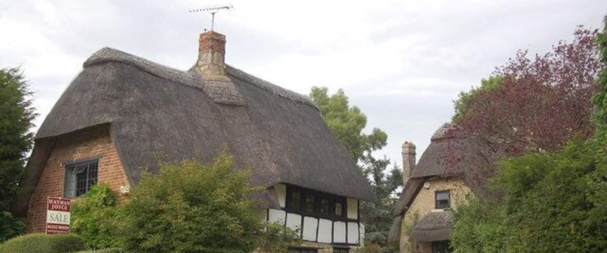 A thatched-roof house with a sign indicating it's for sale.