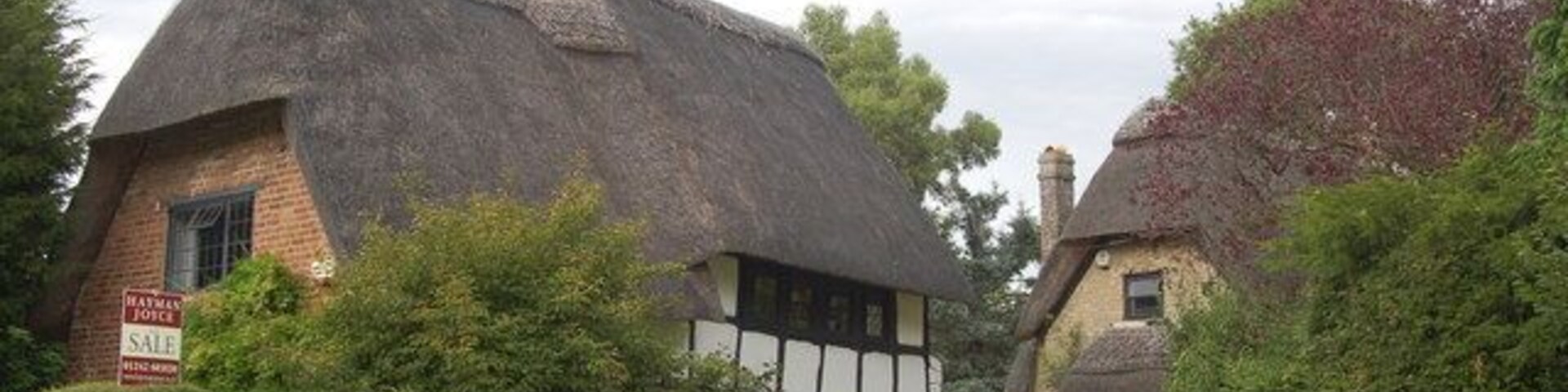 A thatched-roof house with a sign indicating it's for sale.