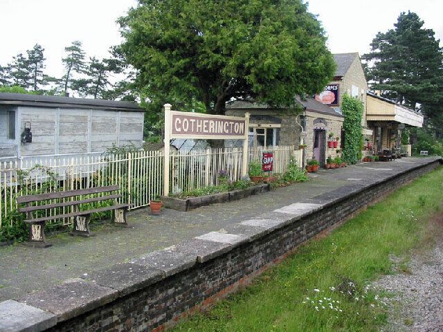 A small station named Cotherington with a signboard, a white fence, and a building with a signboard.
