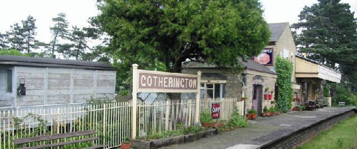 A small station named Cotherington with a signboard, a white fence, and a building with a signboard.