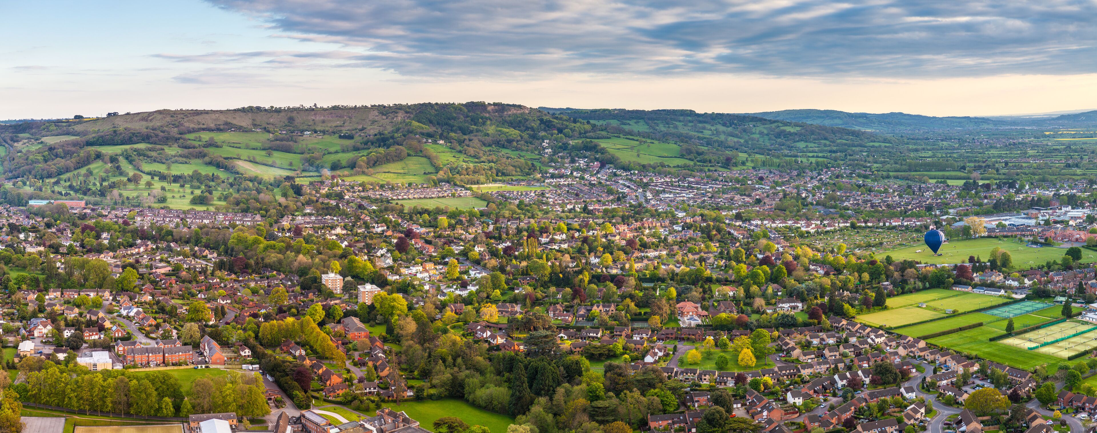 A town nestled in rolling hills with a mix of residential and commercial buildings, surrounded by green fields and trees.
