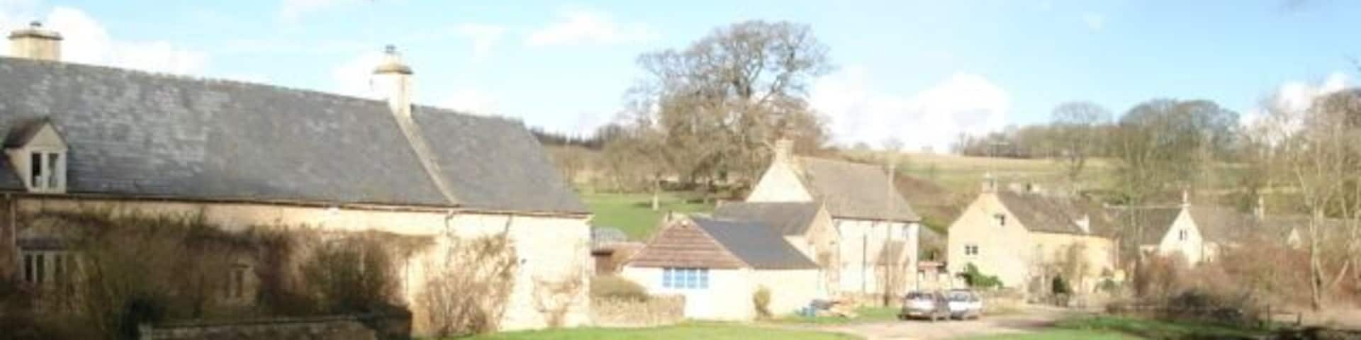 A rural landscape with a narrow stream, stone houses, and a grassy path.