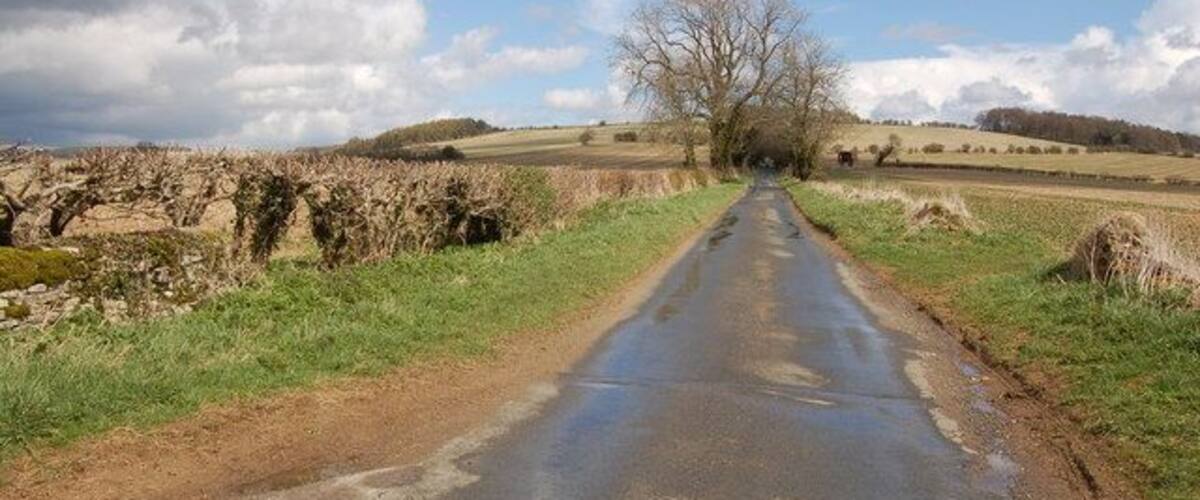 A rural road with stone walls and fields.
