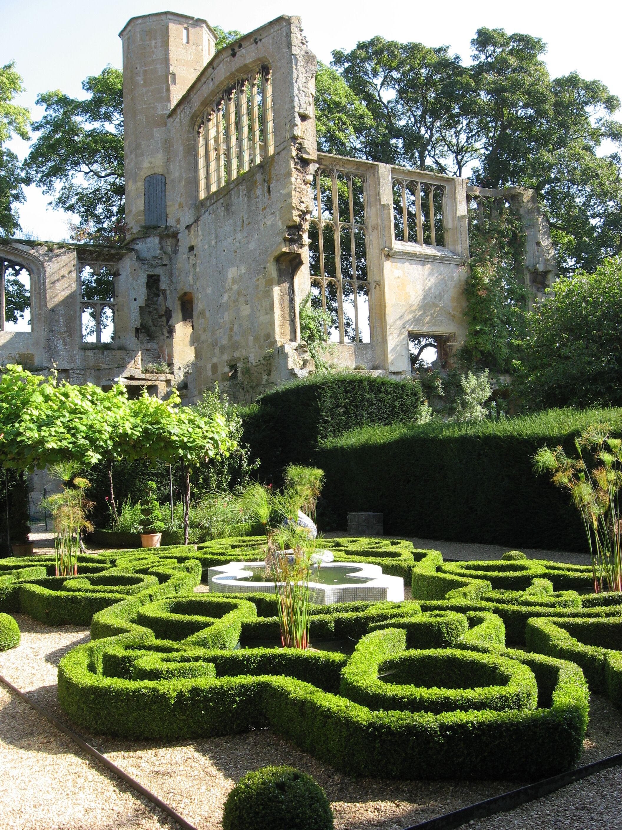 A historic stone building with intricate window designs, surrounded by a well-manicured garden with geometric hedge mazes.