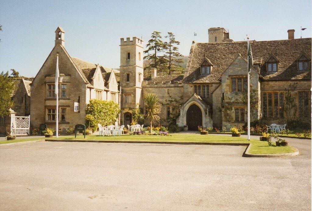 A historic stone building with a large arched entrance, a tower, and a well-maintained lawn.