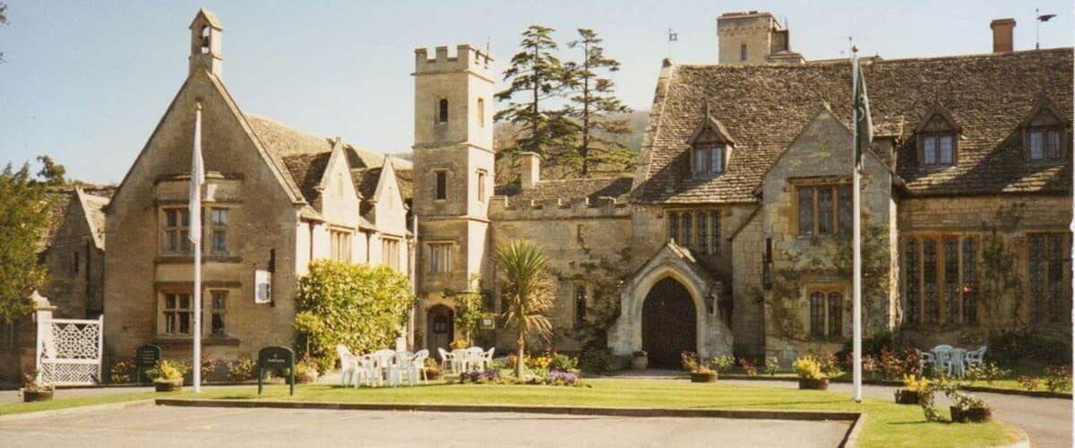 A historic stone building with a large arched entrance, a tower, and a well-maintained lawn.