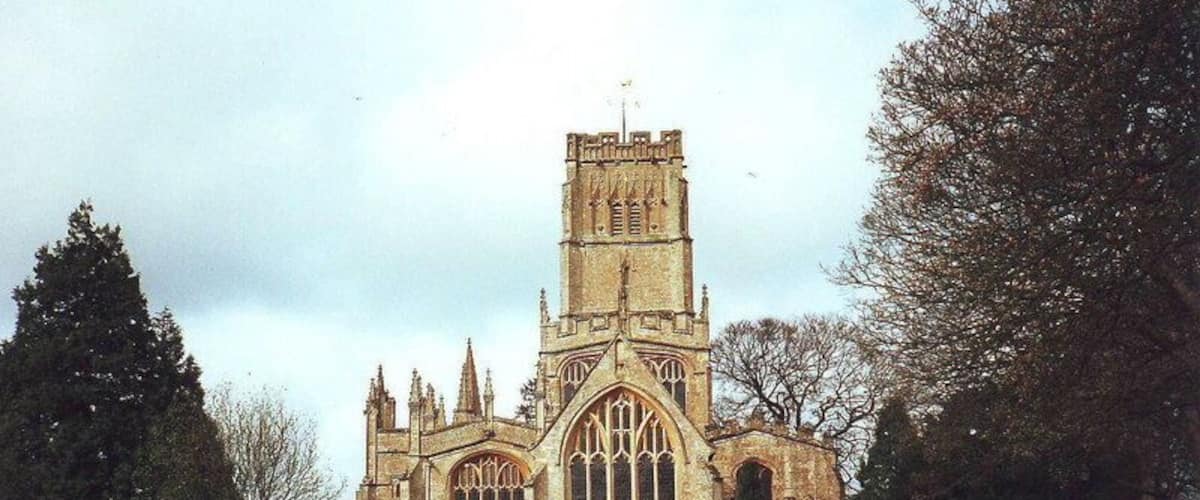A Gothic-style church with a tall tower and large arched windows, surrounded by a cemetery with numerous headstones.