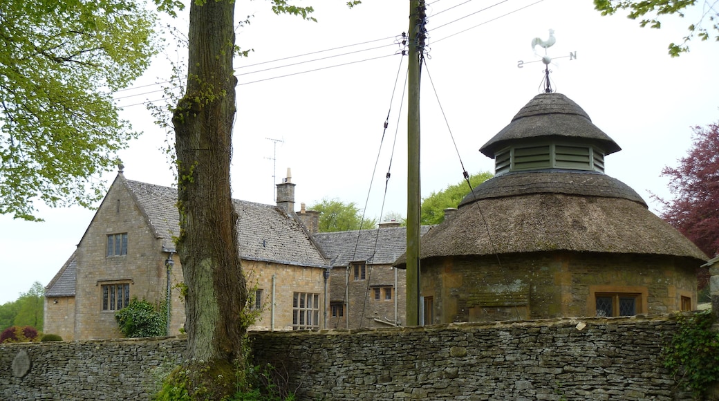 Notgrove Manor. The manor is seen from the churchyard. The octagonal thatched building is a former dairy that is listed grade II.