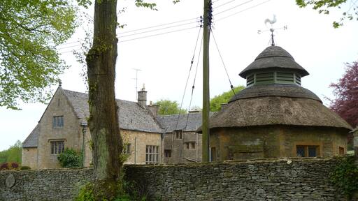 Notgrove Manor. The manor is seen from the churchyard. The octagonal thatched building is a former dairy that is listed grade II.