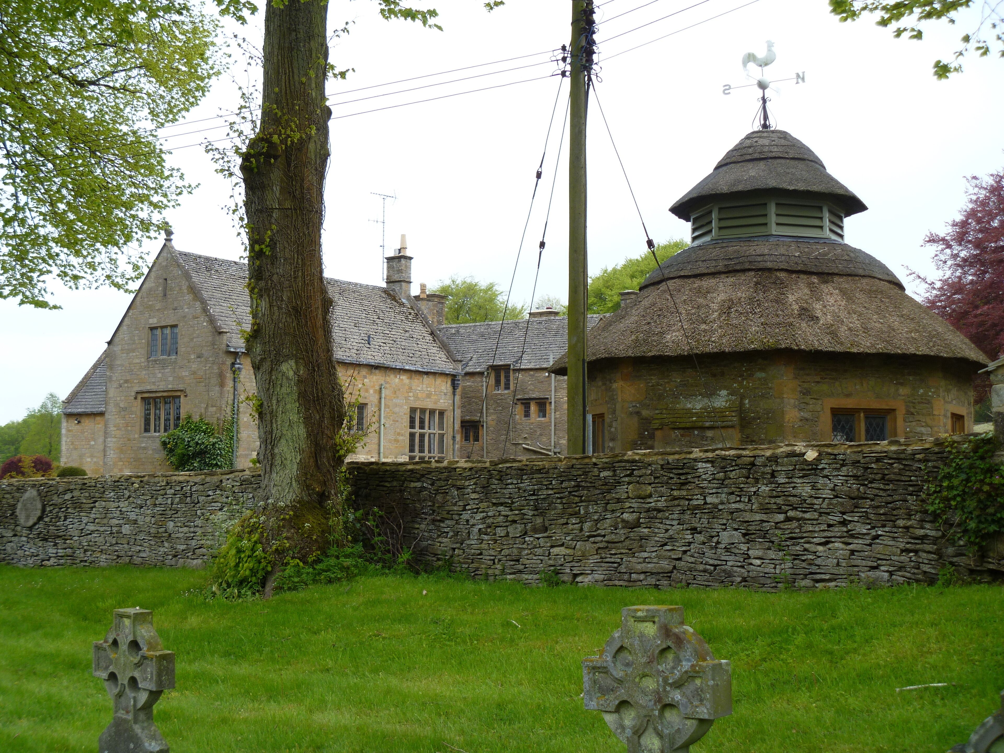 A stone house with a thatched roof, surrounded by a stone wall and a grassy field.