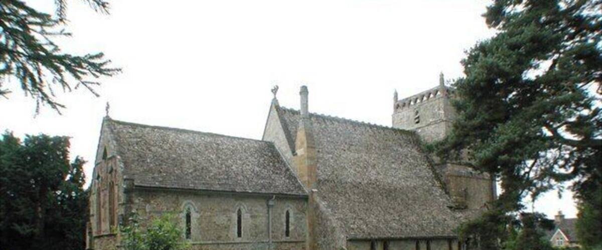 A stone church with a thatched roof, surrounded by a cemetery with gravestones.