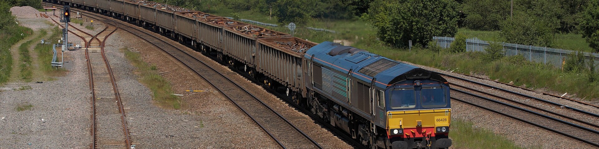 Um trem sobre trilhos de ferrovia, com várias vias, cercado por vegetação e colinas.