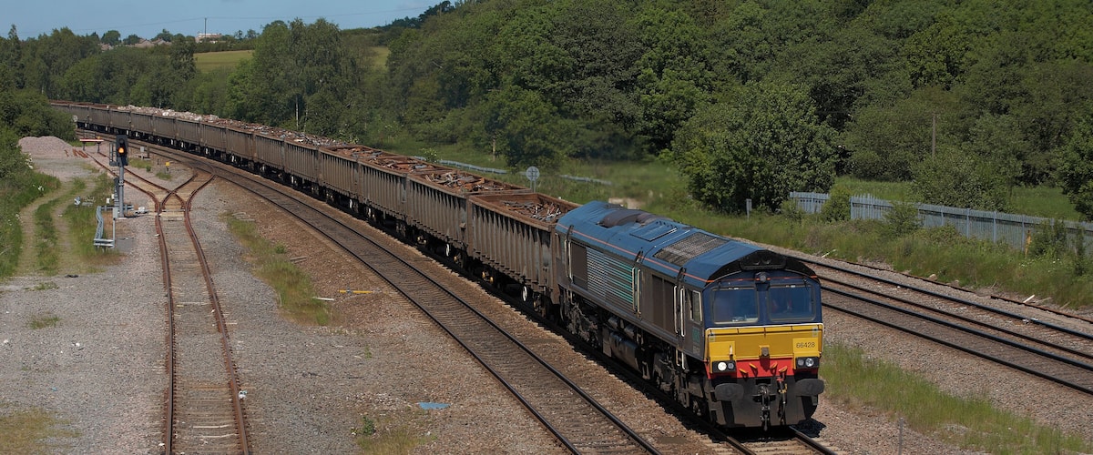 A train on a railway track with multiple tracks, surrounded by greenery and hills.