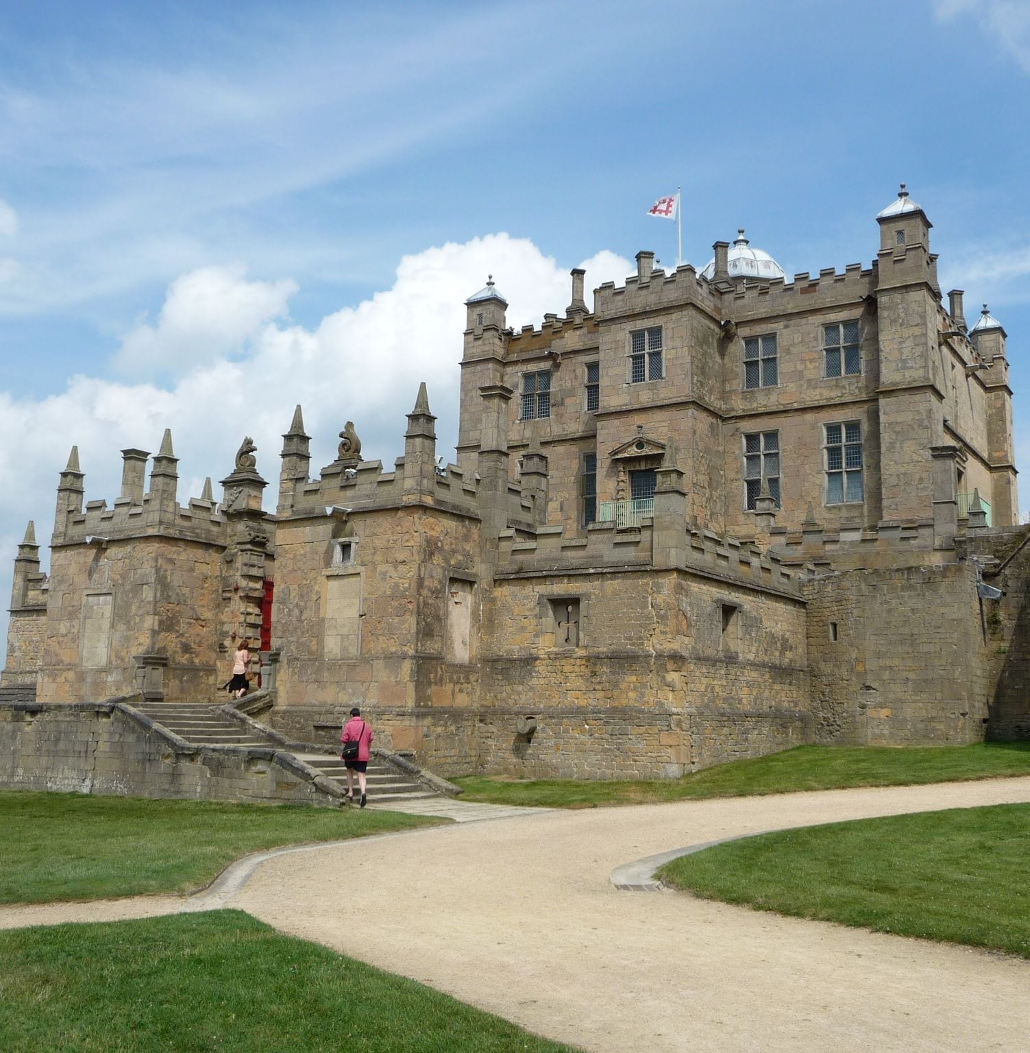 A historic castle with a prominent entrance, a flag, and a pathway leading to the main building.