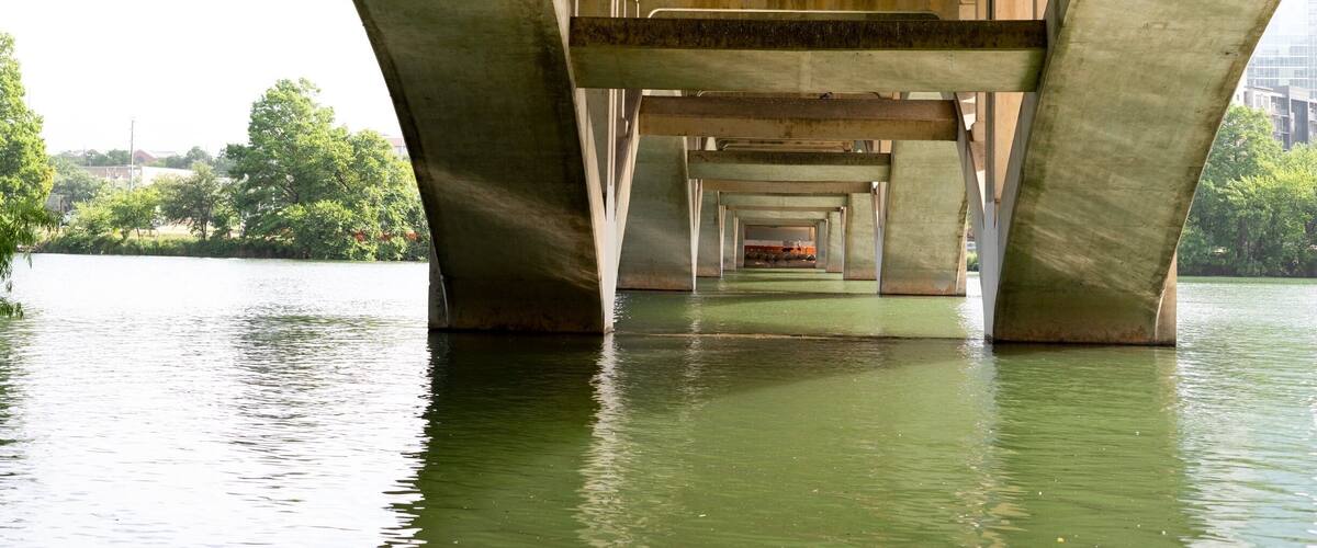 A concrete bridge over a body of water with greenery in the background.
