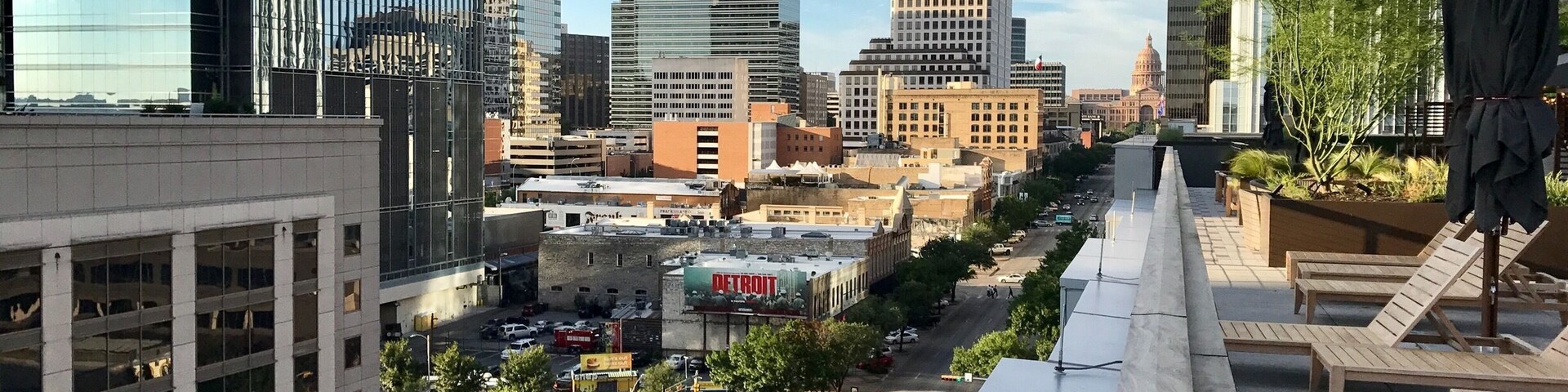 Un paisaje urbano con rascacielos modernos, una calle con coches y un cartel de Detroit.