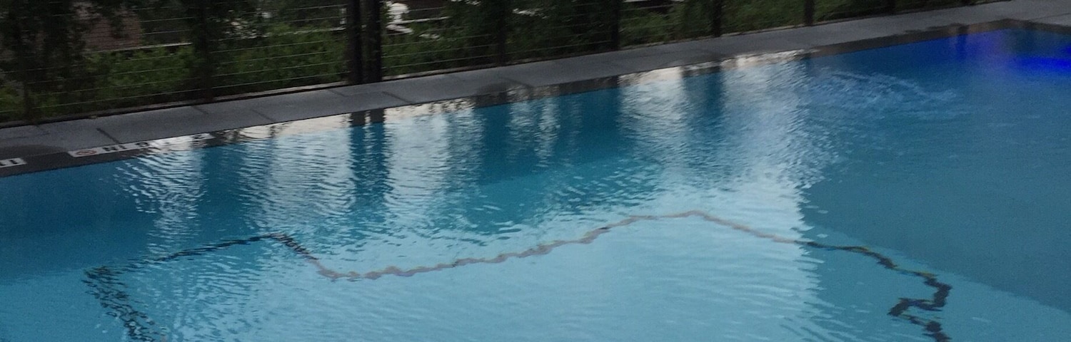 Piscina en la azotea con vistas a edificios de la ciudad y un cielo nublado.
