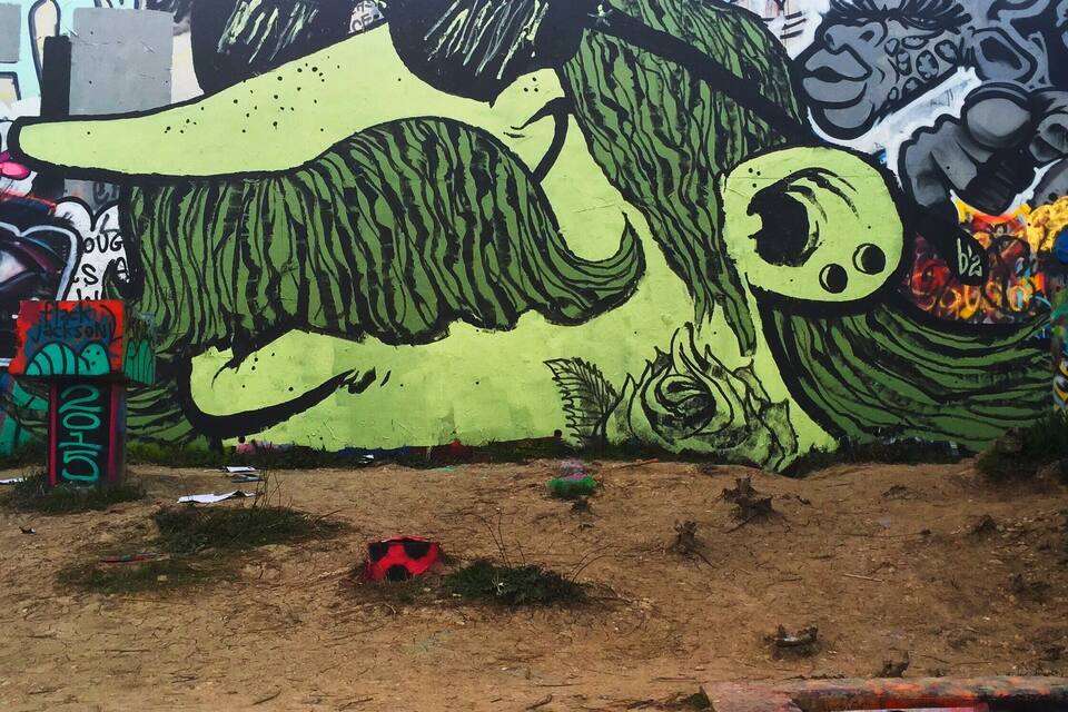 Un ampio murale di graffiti raffigura una creatura verde con un occhio gigante su una parete.