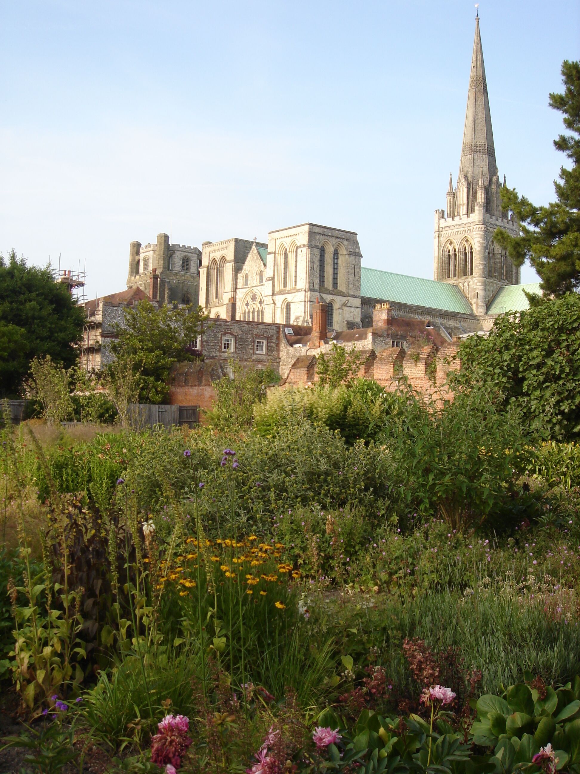 A historic church with a tall spire, surrounded by lush greenery and flowering plants.