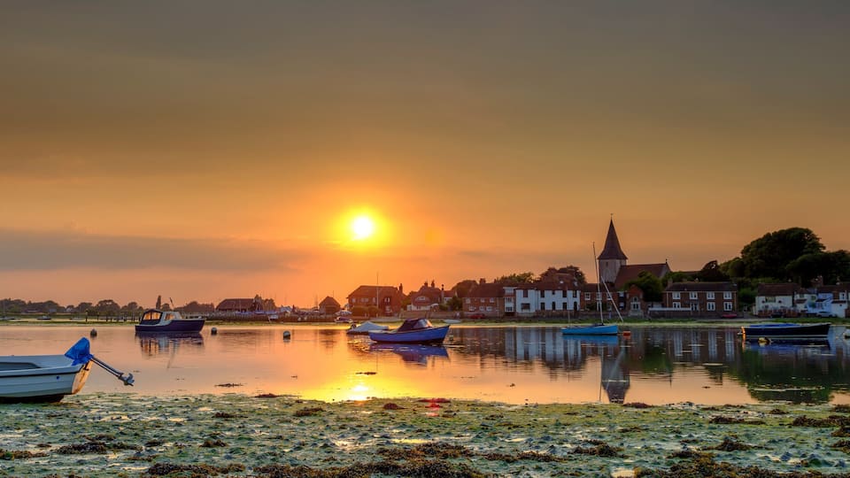 A sunset over a calm lake with boats and houses along the shore.