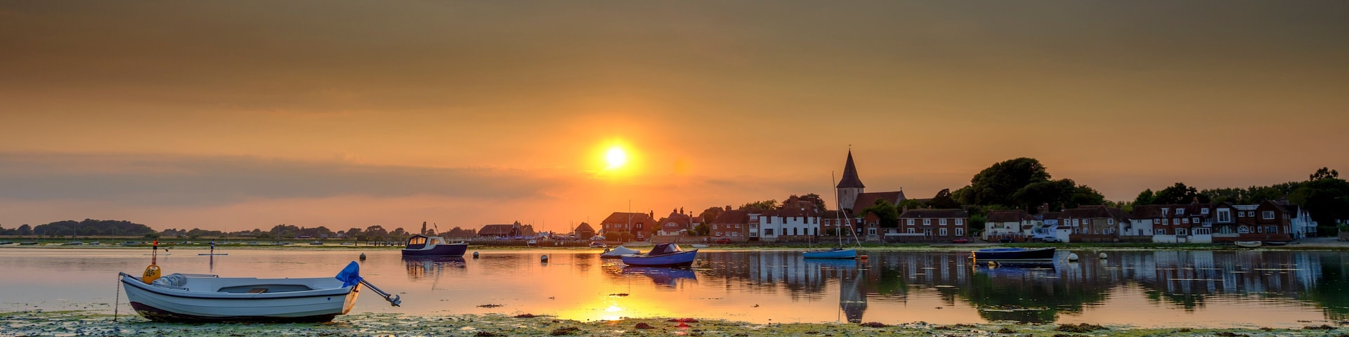 A sunset over a calm lake with boats and houses along the shore.