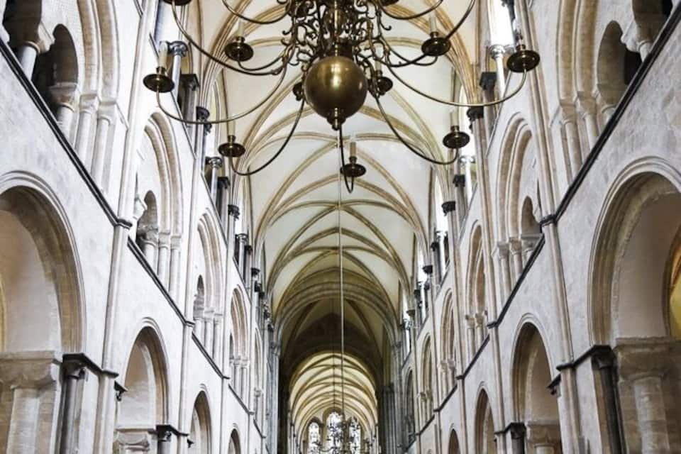 A cathedral interior with arched ceilings, rows of wooden pews, and a large chandelier.