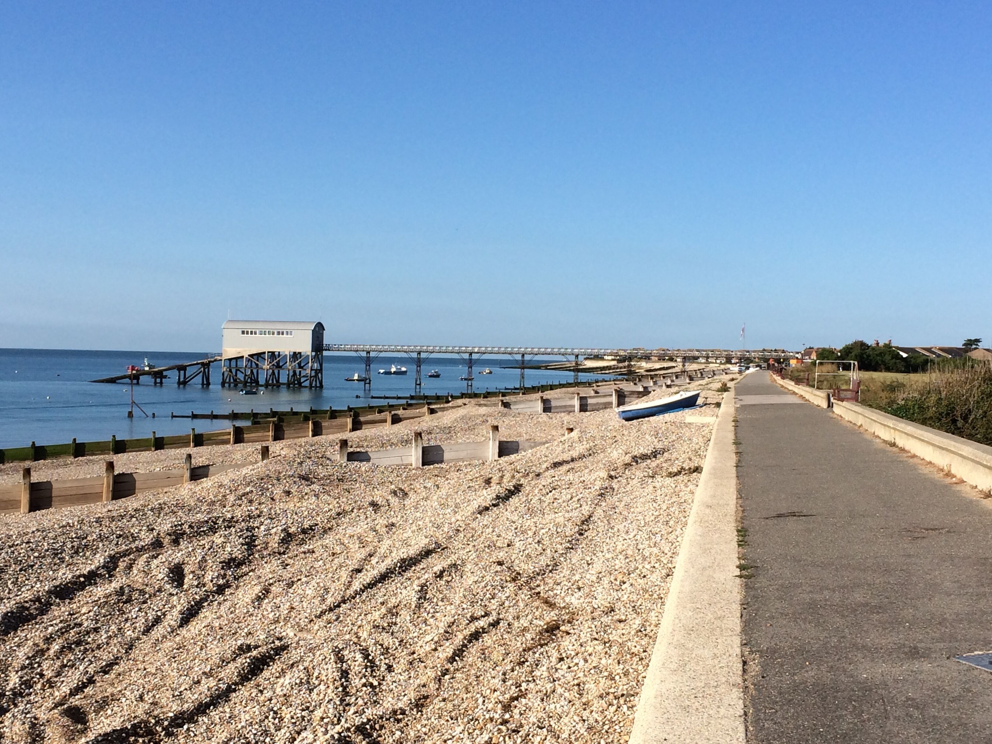 A coastal road with a rocky beach, a pier, and boats in the water.