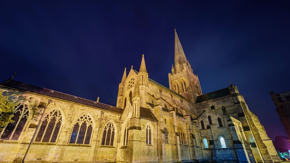 A historic cathedral with pointed arches and a tall spire, illuminated at night.