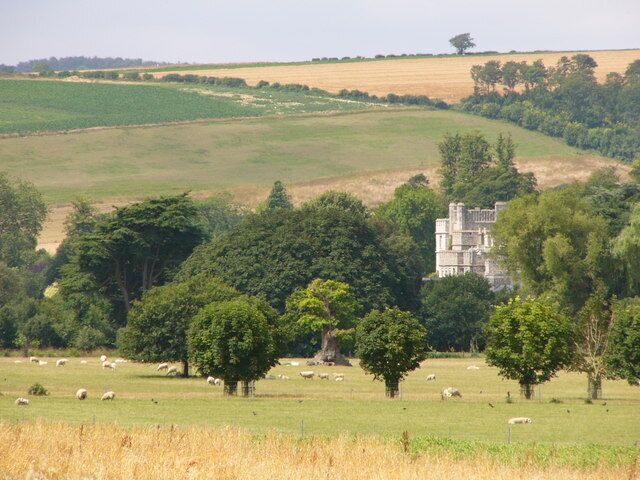 Paisaje rural con colinas onduladas, una construcción similar a un castillo y ovejas pastando.