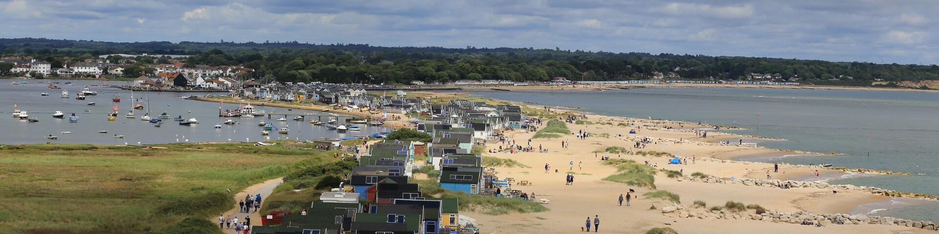 A coastal town with a sandy beach, a marina with boats, and houses along the shore.