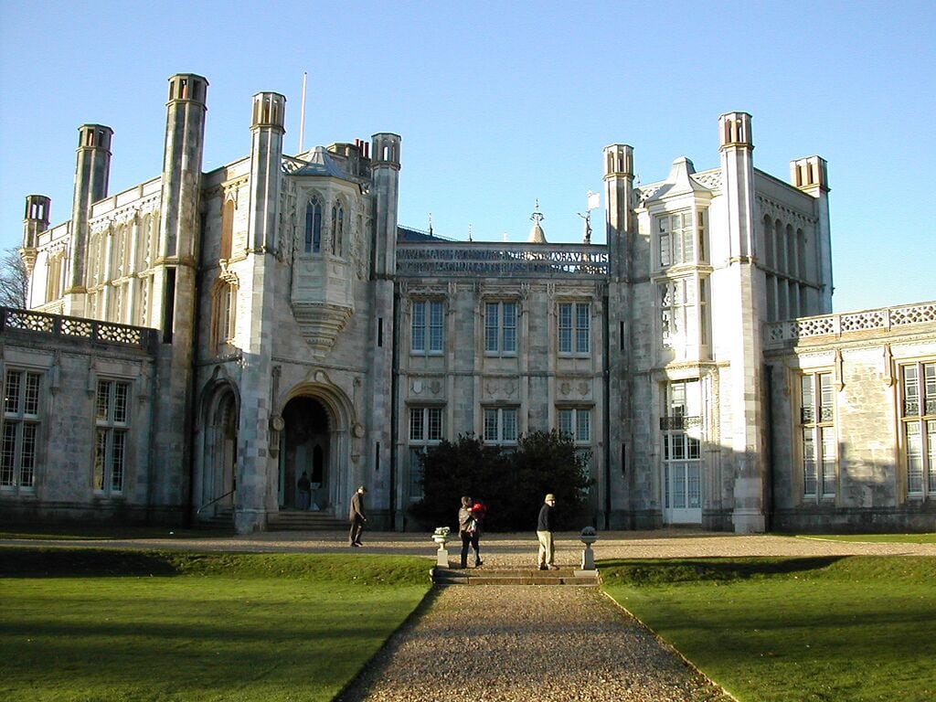 A large historic building with multiple chimneys, a central entrance with steps, and a well-maintained lawn.