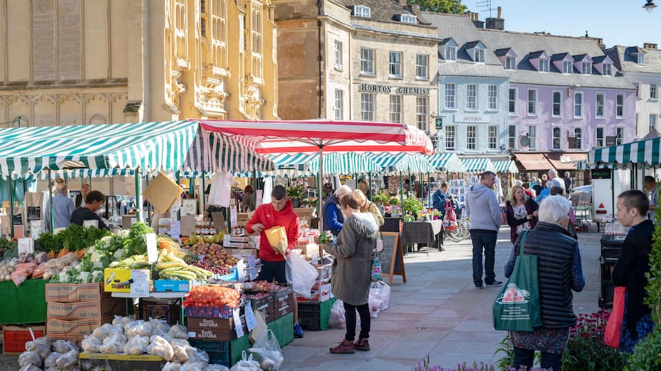 A bustling outdoor market with vendors selling fresh produce under striped umbrellas.