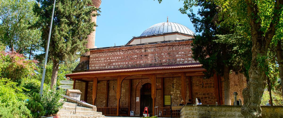 A historic building with a dome and a minaret, surrounded by trees and a cobblestone path.