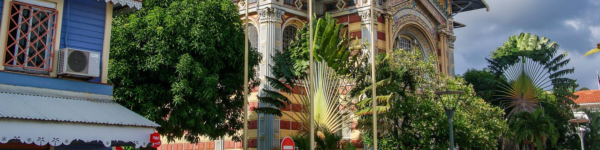 A historic building with ornate architecture, multiple flags, and lush greenery.