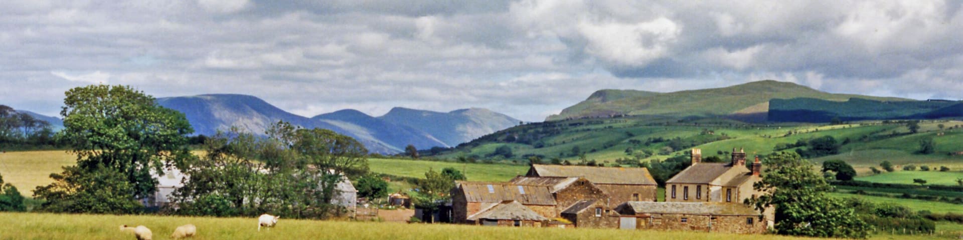 Eastward towards Ennerdale from near Cleator Moor. A fine panorama of the mountains around Ennerdale, seen from just off the B5294 Cleator - Frizington road at Threapthwaite. To the left is Murton Fell (1,461 ft.), Blake Fell (1,626 ft.), then Great Borne (2,018 ft.) and Starling Dodd (2,077 ft.) shining in sunlight NE of Ennerdale Water, while rather nearer on the right is Grike (1,556 ft.) joined to the Ennerdale Fells which line the south side of Ennerdale Water.
