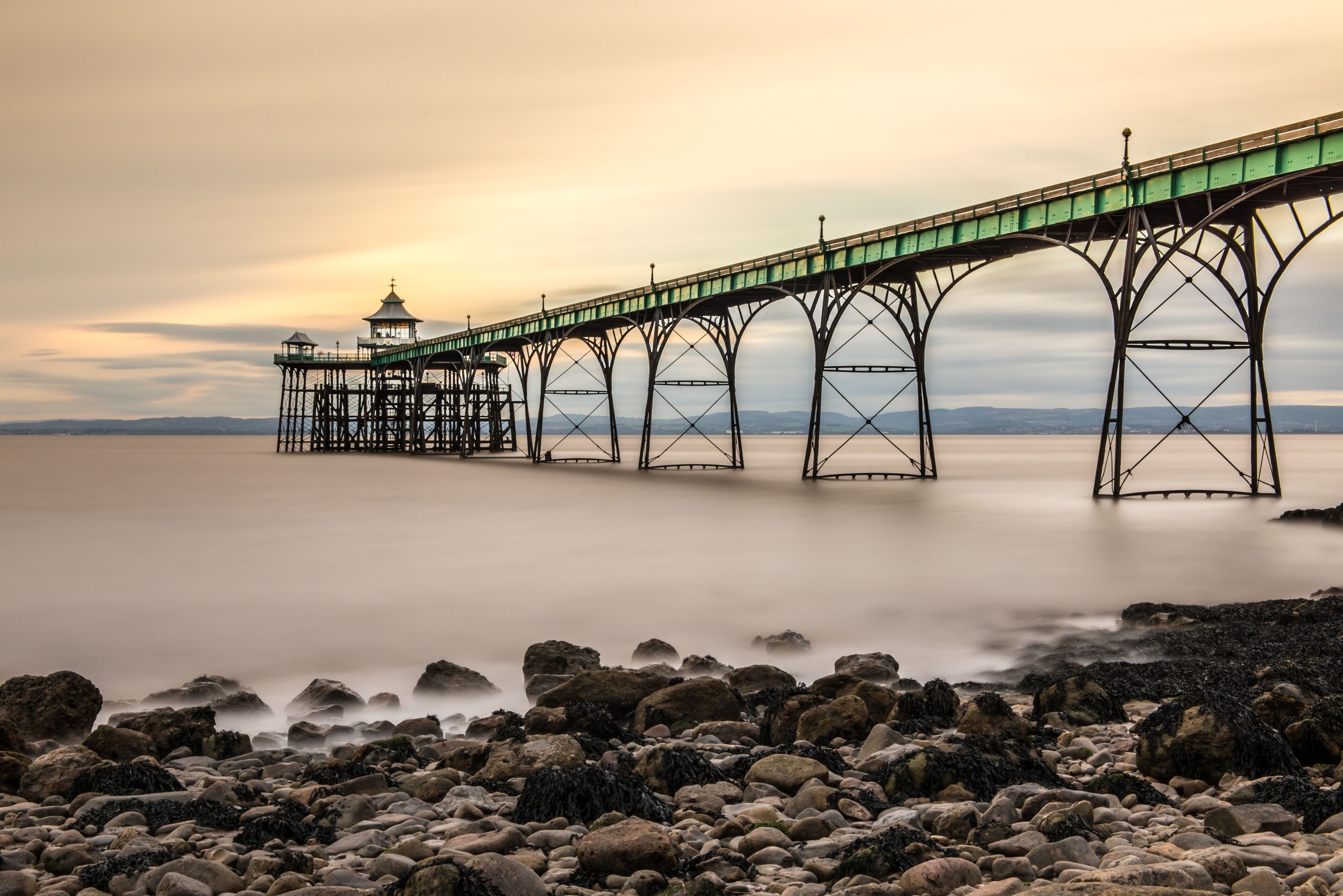 A pier extending over calm water with a rocky shoreline in the foreground.