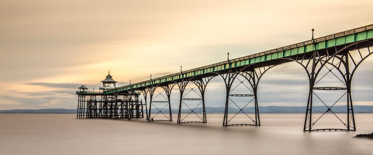 A pier extending over calm water with a rocky shoreline in the foreground.
