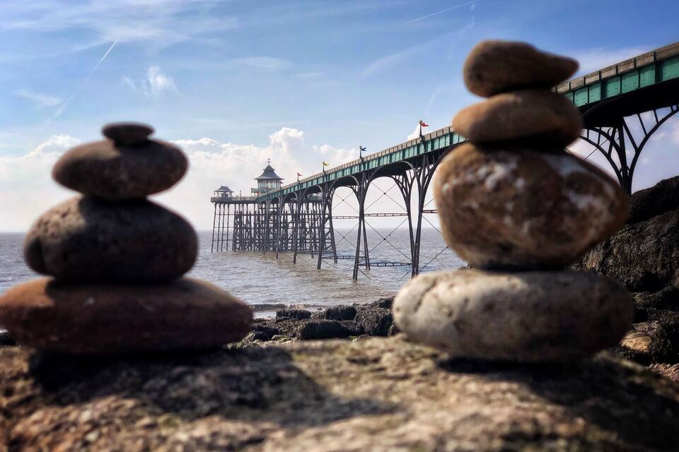 A stack of rocks in the foreground with a pier extending into the water in the background.