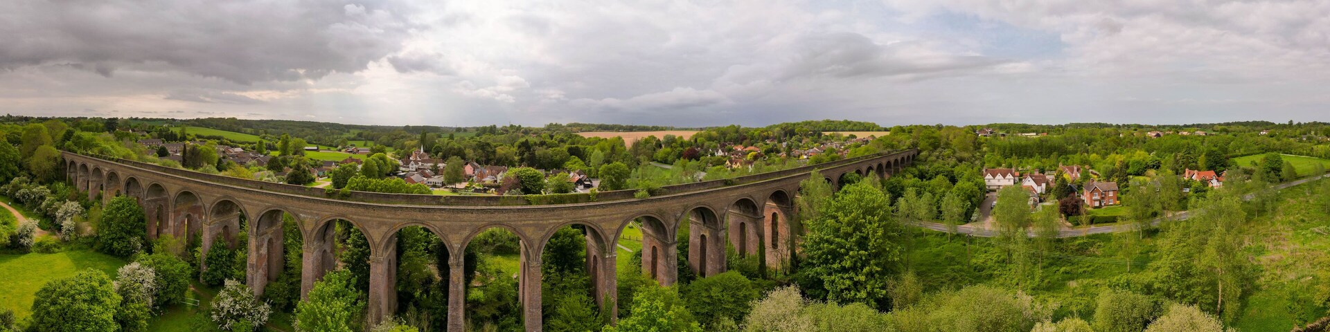 Un viaducto de piedra sobre un valle verde y exuberante con casas y árboles.