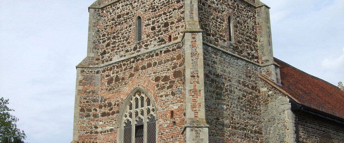 A historic stone church with a tall bell tower, arched windows, and a red-tiled roof.