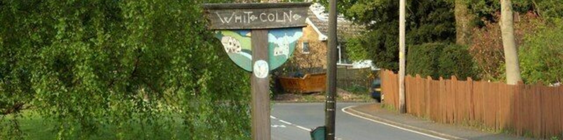 Um sinalizador com a palavra 'WHITCOLN' escrita, rodeado por vegetação e uma estrada.