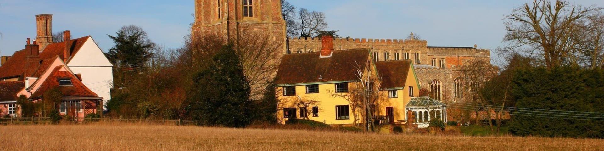 A church with a tall tower, surrounded by houses and a field.