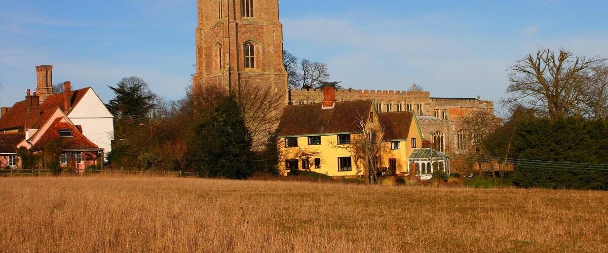 A church with a tall tower, surrounded by houses and a field.