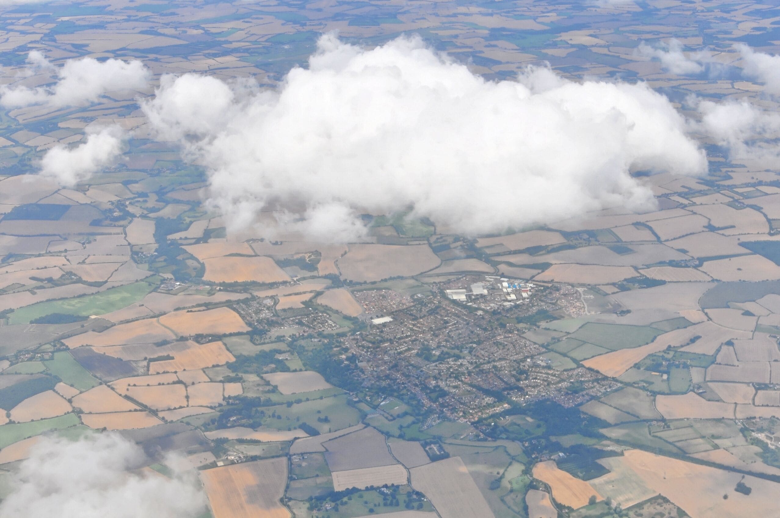 An aerial view of a rural landscape with fields, a small town, and a large cloud formation.