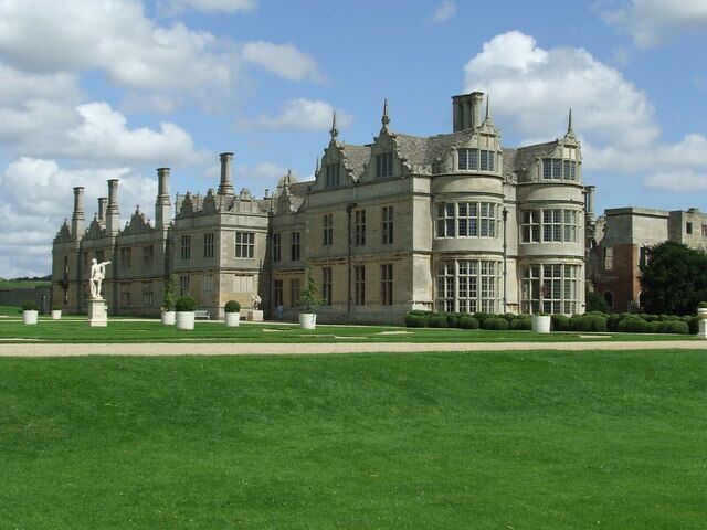 A large, historic building with a symmetrical facade, multiple chimneys, and a well-manicured lawn.