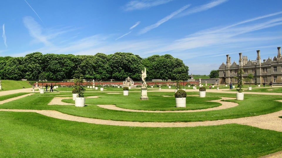A formal garden with manicured lawns, geometric pathways, and classical statues.
