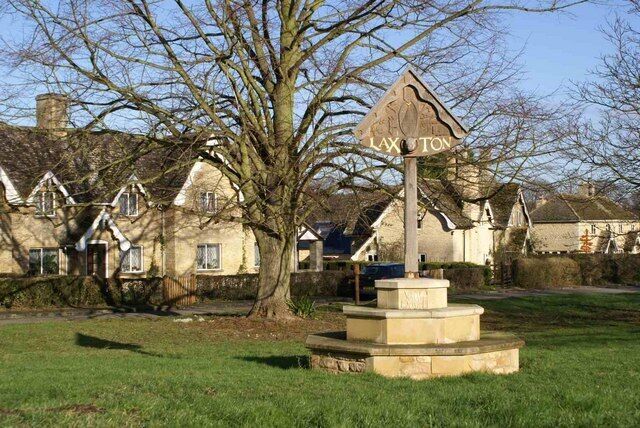 A stone monument with 'LAXTON' inscribed, surrounded by a grassy area and houses in the background.