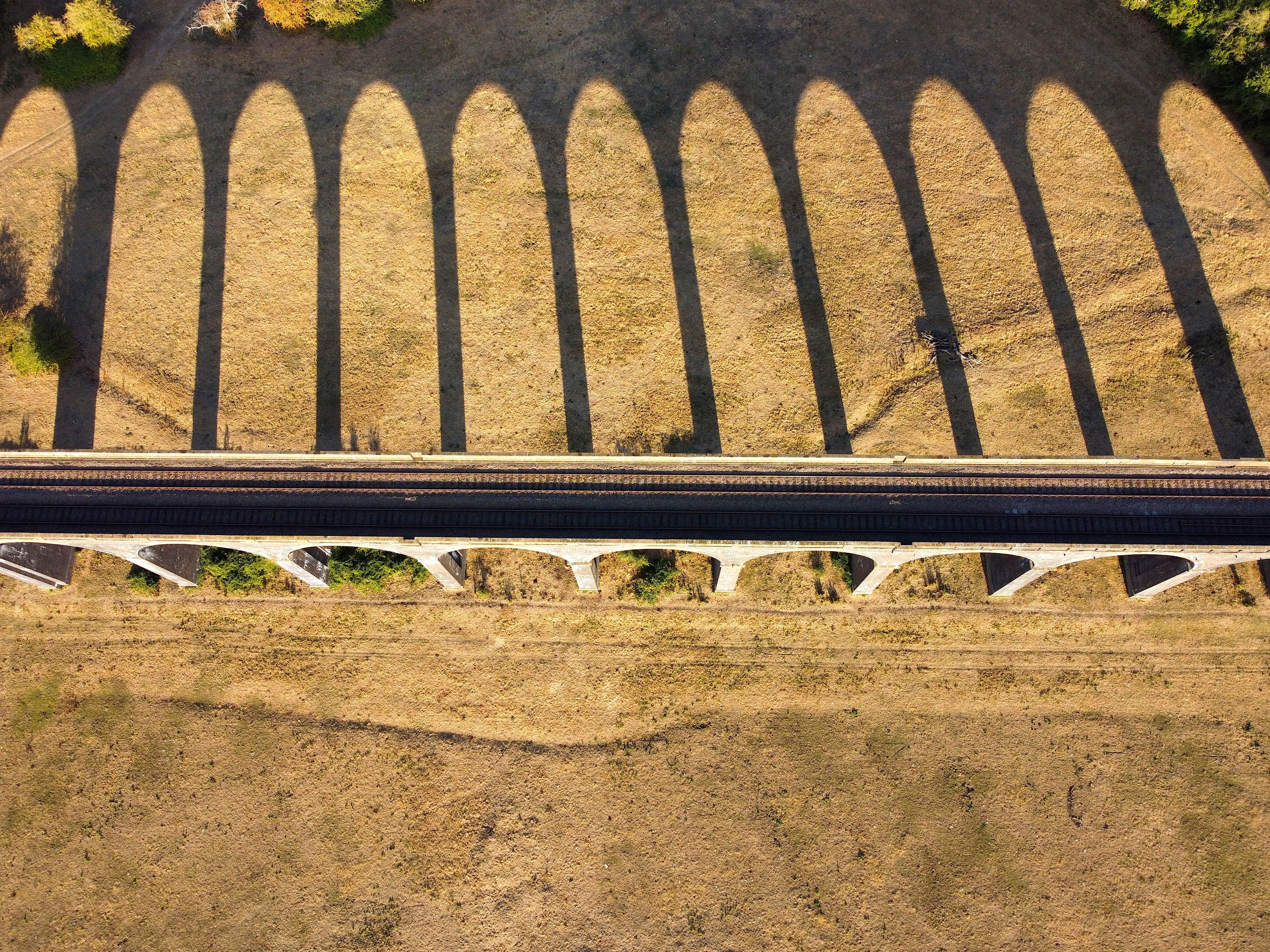Aerial view of Welland Viaduct with its long series of arches casting dramatic shadows across the dry grassy fields in the English countryside, Corby, England, United Kingdom.