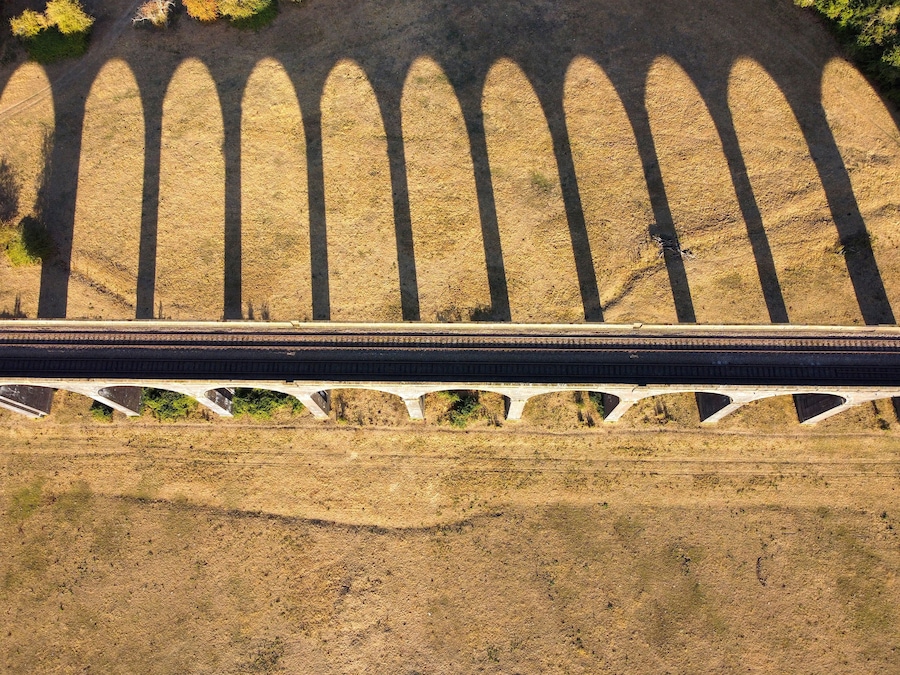 Aerial view of Welland Viaduct with its long series of arches casting dramatic shadows across the dry grassy fields in the English countryside, Corby, England, United Kingdom.