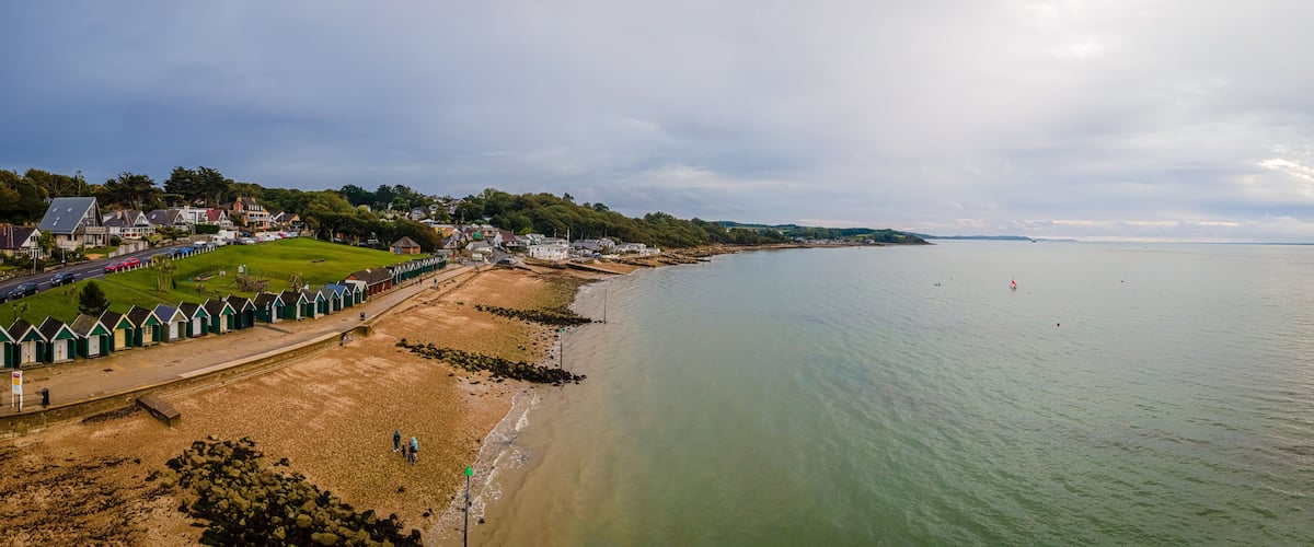 A coastal town with a sandy beach, green-roofed beach huts, and a calm sea.